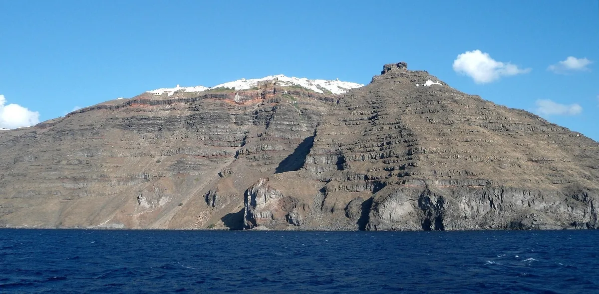 The layered caldera cliffs of Santorini with Skaros Rock and the white houses of Imerovigli on the rim, seen from the sea