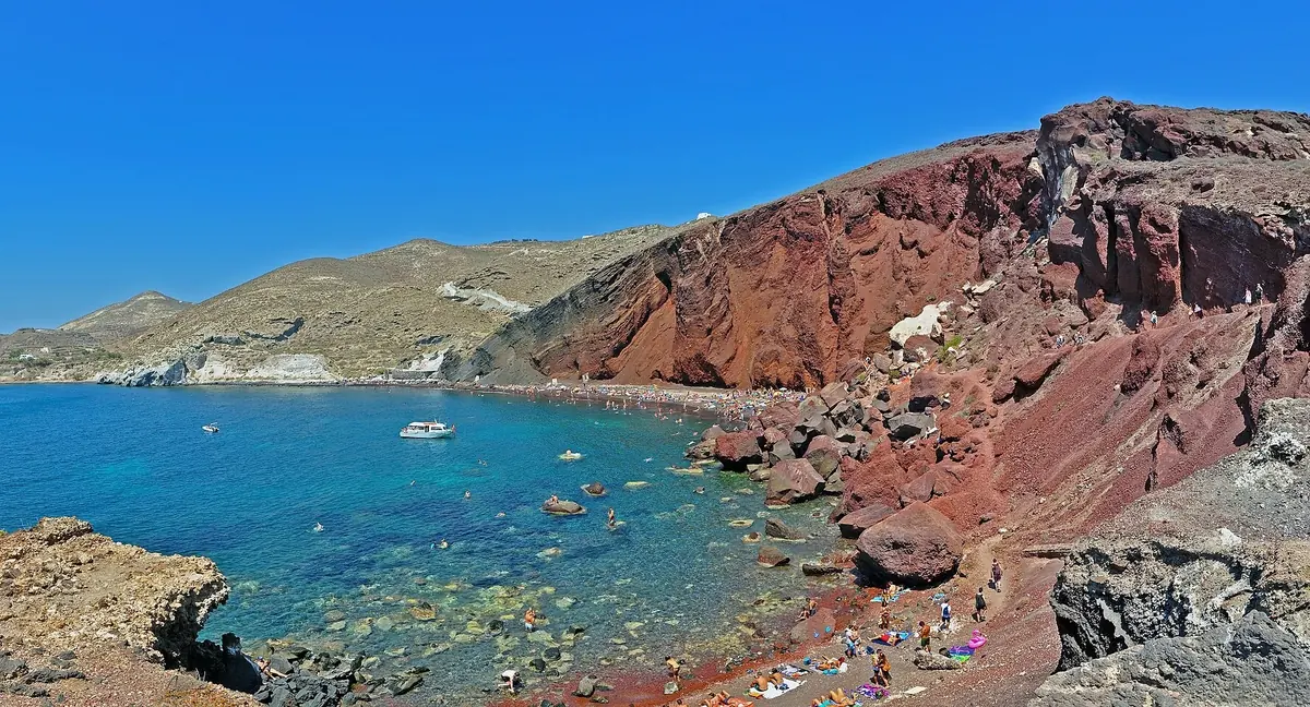Red volcanic cliffs above the dark sand and clear blue water of Red Beach on Santorini