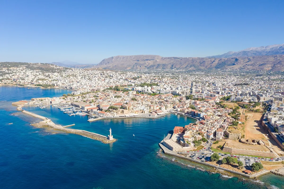 Aerial view of Chania's Venetian harbour, lighthouse breakwater and old town on Crete, with mountains behind