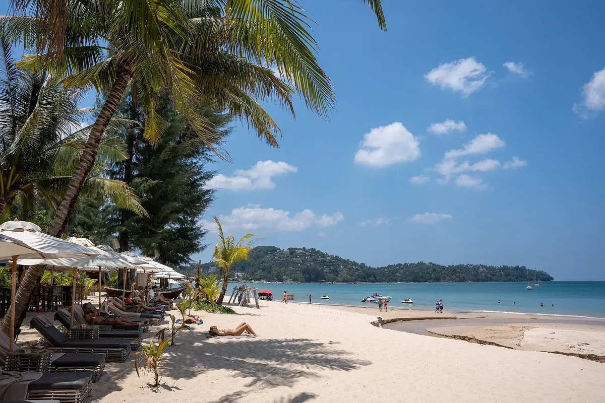 Coconut palms and beach loungers on the white sand of Bang Tao Beach on Phuket, with a green headland beyond