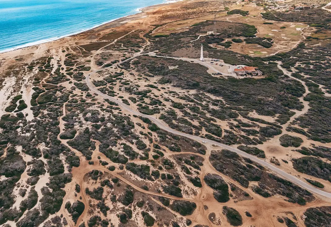Aerial view of the California Lighthouse amid sandy scrubland and trails on Aruba's northwest tip, with the sea beyond