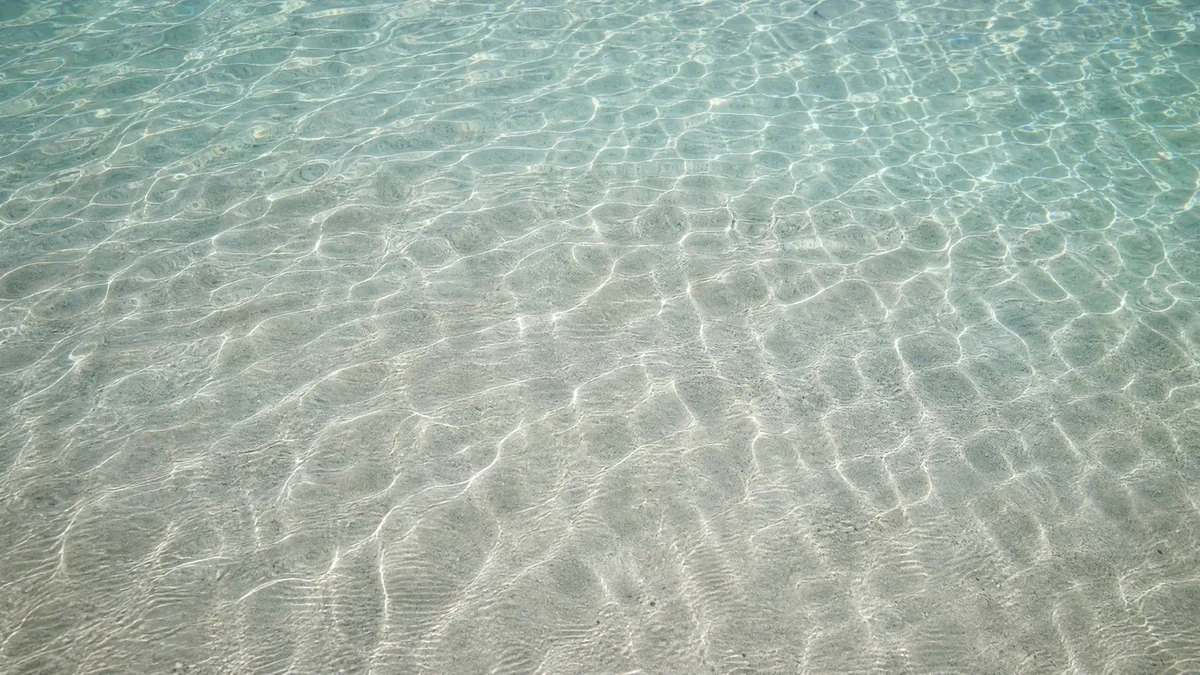 Looking straight down through very clear shallow water at rippled white sand and light patterns