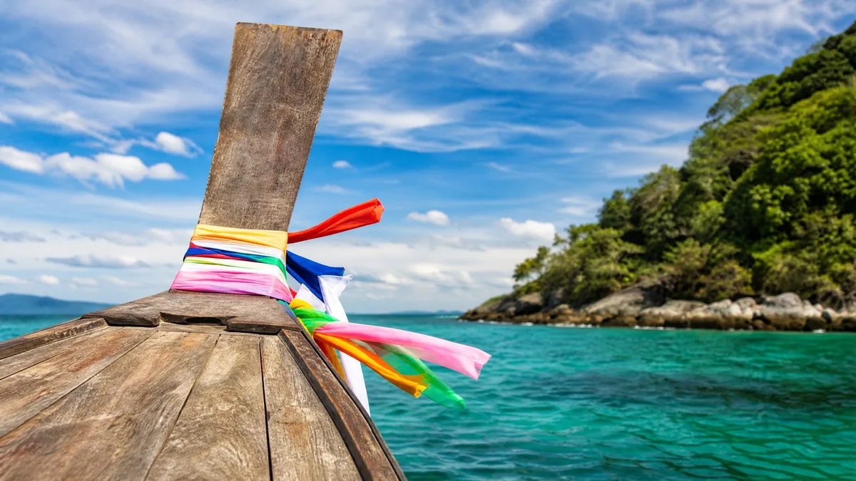 The upturned wooden bow of a traditional longtail boat decorated with colorful cloth ribbons, turquoise water around it