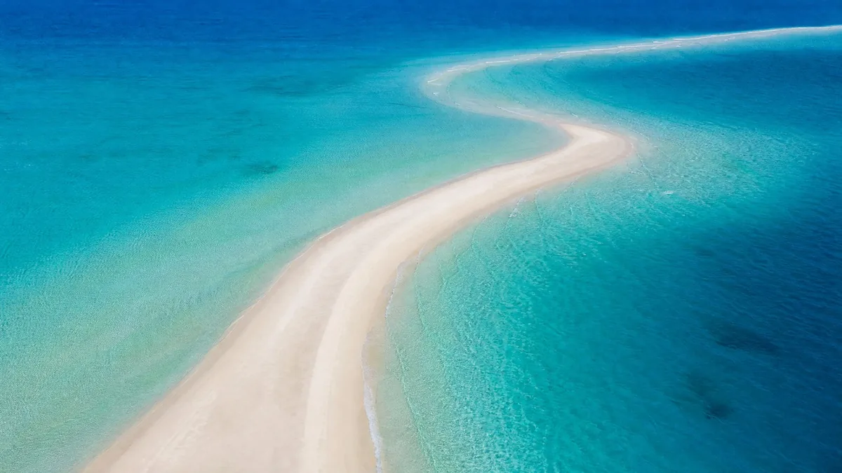Aerial view of a curving white sandbar between shades of turquoise and deep blue water