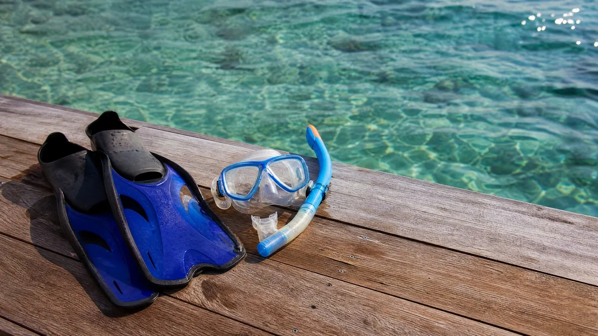A snorkel mask, snorkel and fins laid out on a wooden dock above clear water