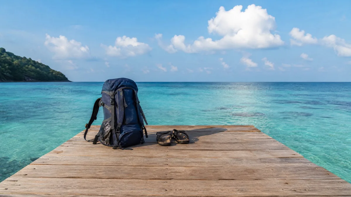 A single travel backpack and a pair of sandals at the end of a wooden pier over turquoise water