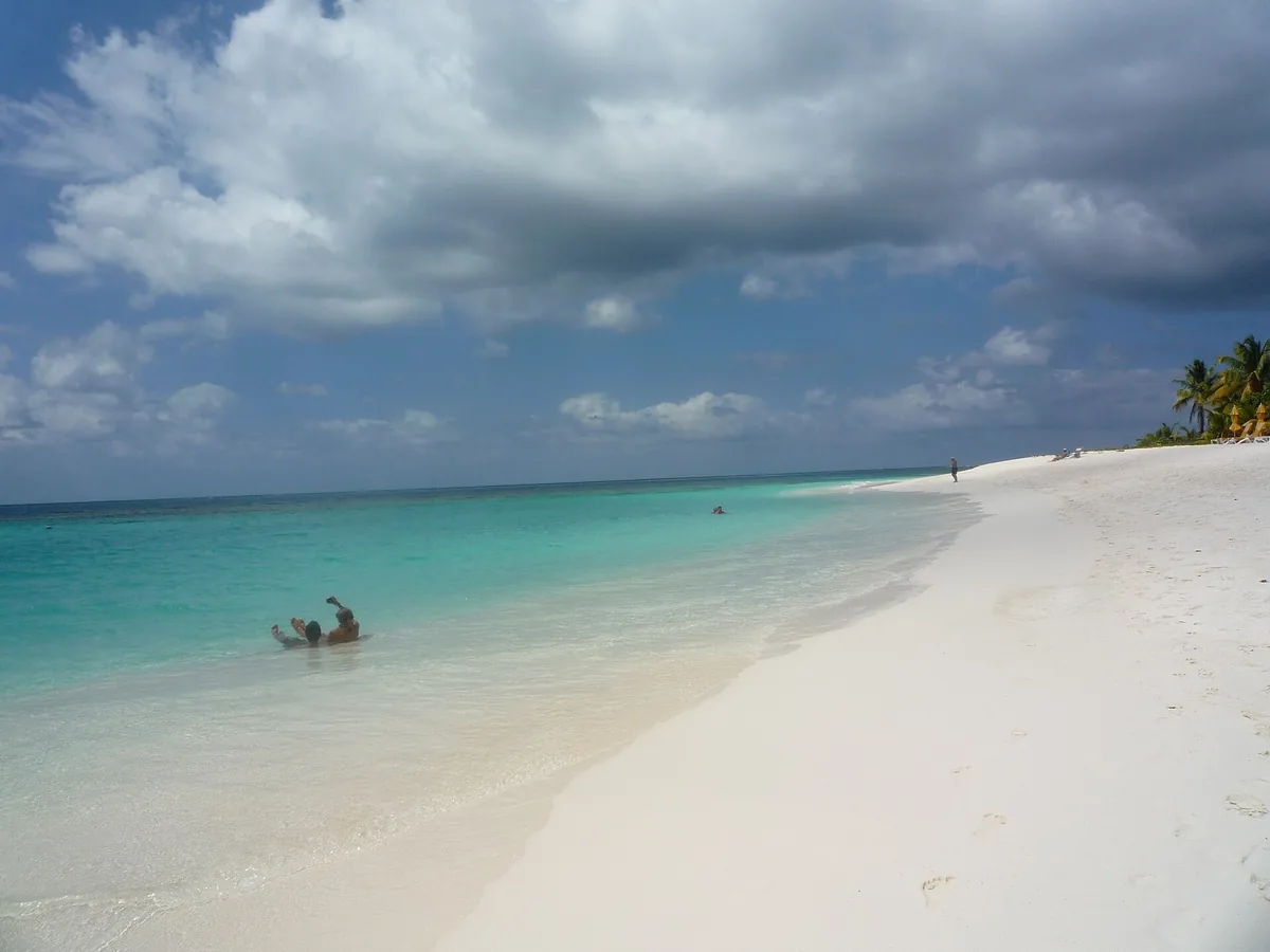 Turquoise water lapping the powdery white sand of Shoal Bay on Anguilla under a cloudy sky