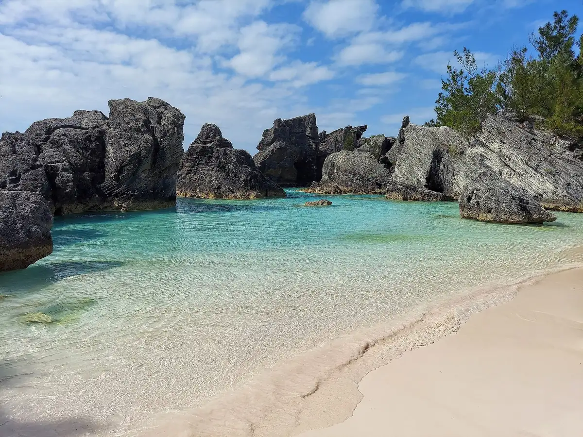 Clear turquoise water and pale pink sand in a small cove ringed by dark limestone rocks at Horseshoe Bay, Bermuda