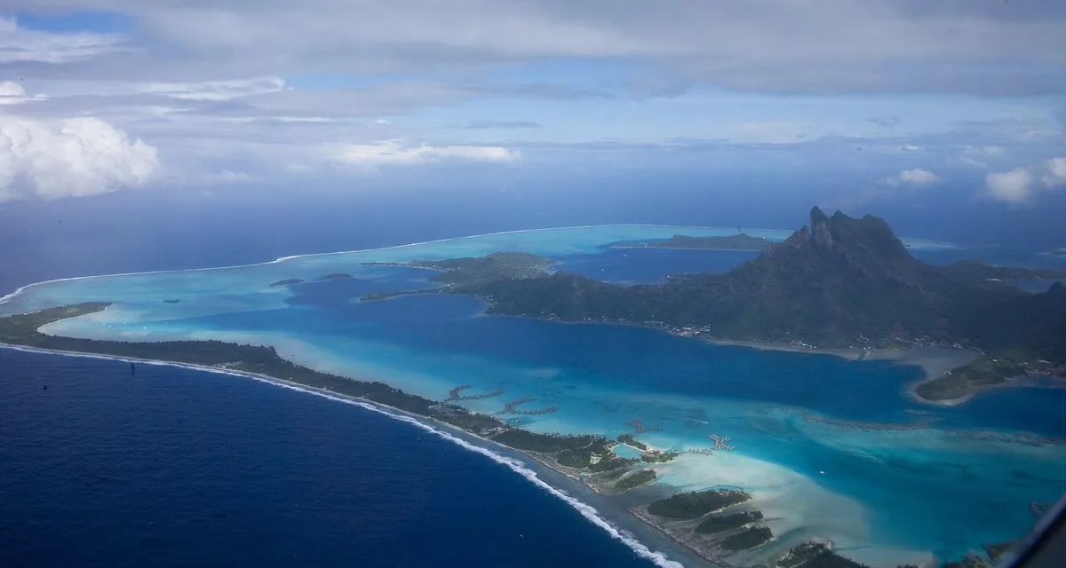 Aerial view of Bora Bora's turquoise lagoon, reef motu and the peak of Mount Otemanu