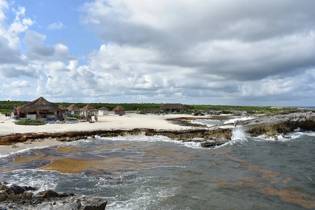 Waves breaking over limestone rocks in front of the beach and palapa huts at Playa El Mirador on Cozumel