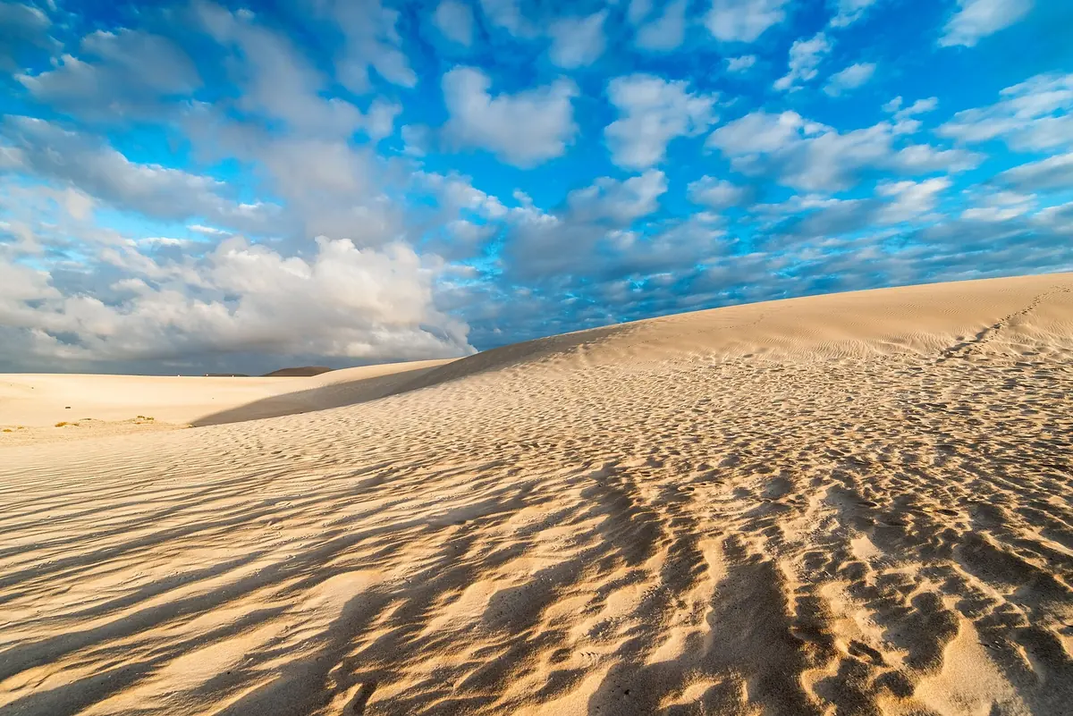 Wind-rippled golden sand dunes at Corralejo on Fuerteventura under a sky of scattered clouds