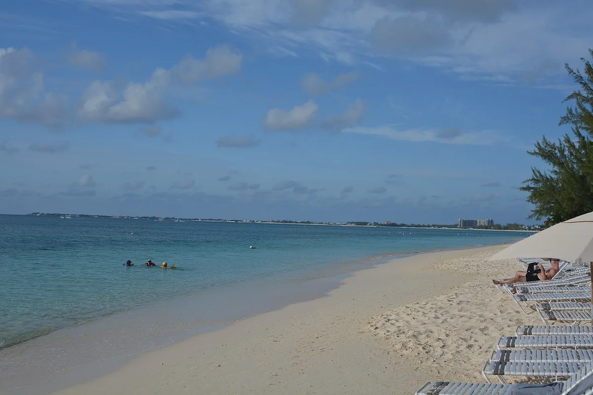 Calm turquoise water along the white sand of Seven Mile Beach on Grand Cayman, with sun loungers in the foreground