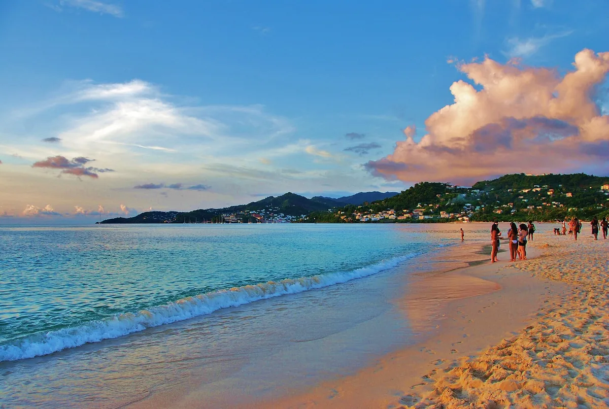 Gentle surf on the golden sand of Grand Anse Beach, Grenada, with the green hills of St. George's behind