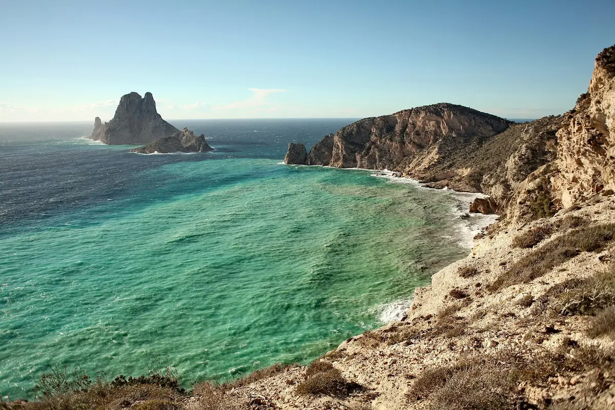 The rocky islets of Es Vedrà and Es Vedranell off a turquoise bay below the cliffs of Ibiza's southwest coast