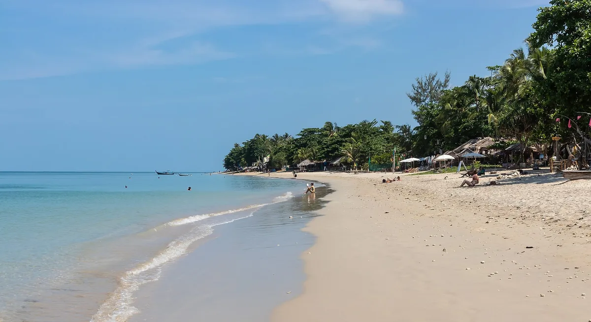 Gentle surf on the long sandy shore of Klong Khong Beach on Koh Lanta, backed by palms and beach huts