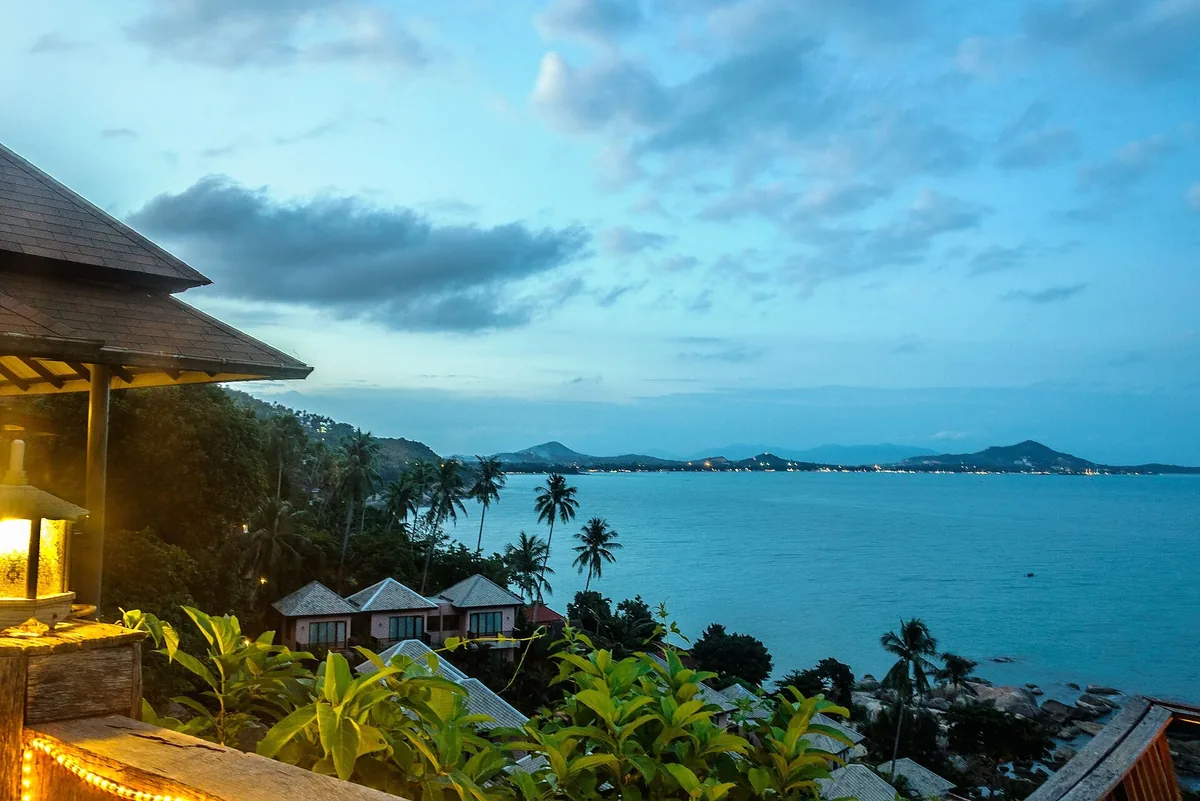 Palm-covered slopes and rooftops above the blue water of Chaweng Bay on Koh Samui at dusk