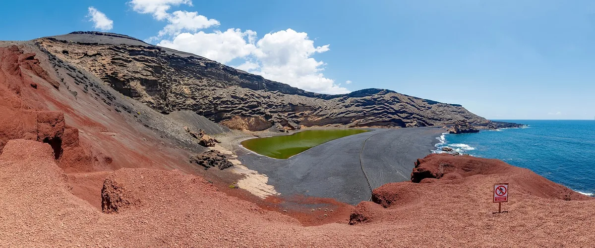 The green lagoon of Charco de los Clicos below the red and ochre cliffs of El Golfo crater on Lanzarote