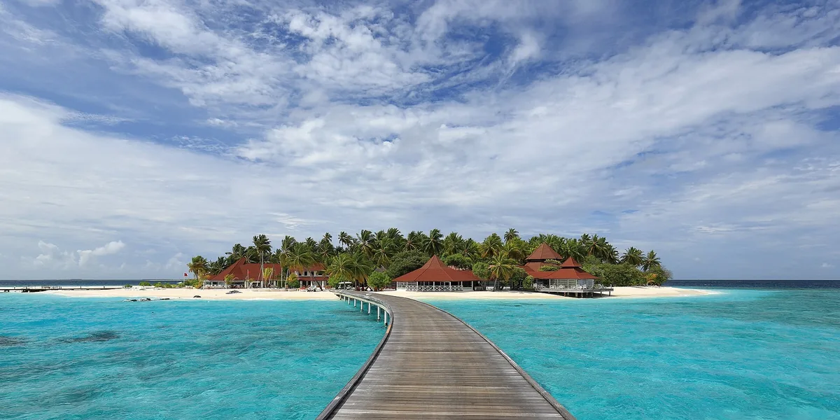 A wooden jetty crossing a turquoise lagoon to the palm-covered resort island of Thudufushi in Ari Atoll, Maldives