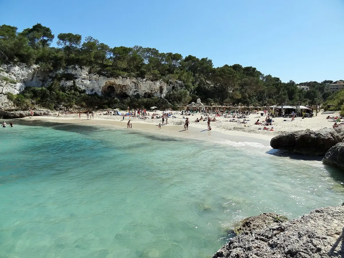 Turquoise water in the narrow cove of Cala Llombards on Mallorca, with a small beach below pine-topped limestone cliffs