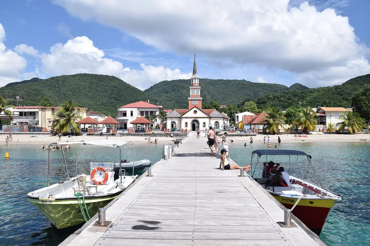 A wooden jetty with moored boats leading to the beach and white church steeple of Les Anses-d'Arlet, Martinique
