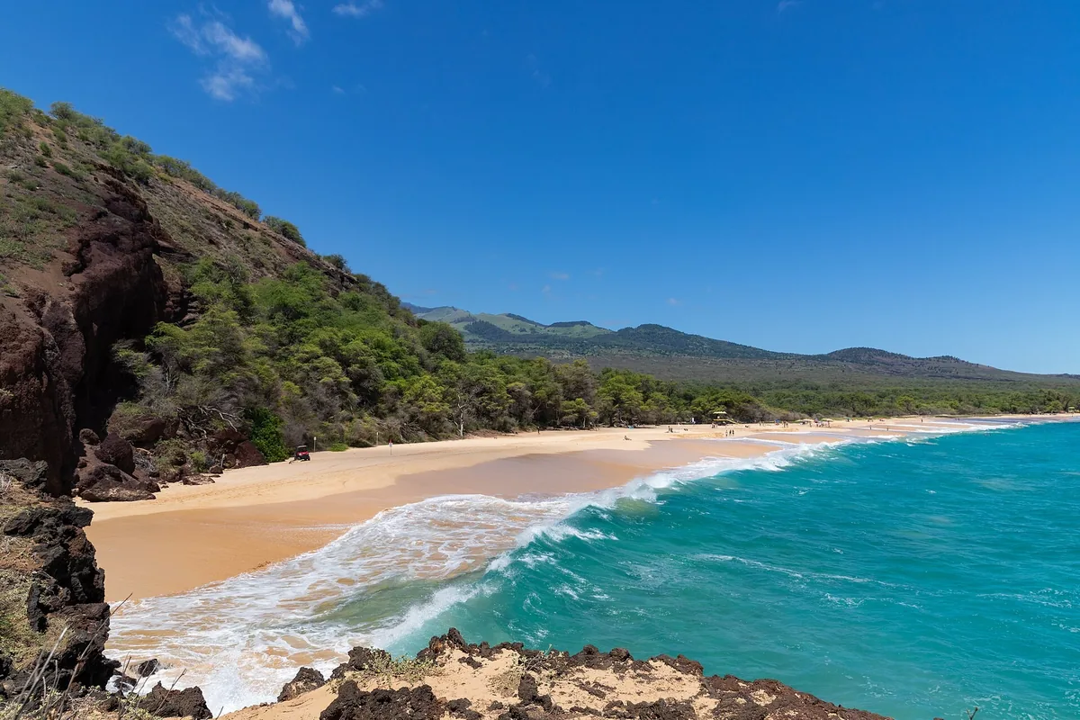 Turquoise surf rolling onto the long golden sand of Makena Beach (Big Beach) below a green hillside on Maui