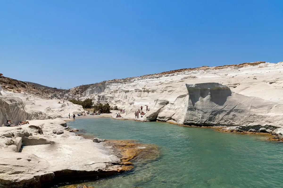 White volcanic rock formations curving around the clear green water of Sarakiniko on Milos
