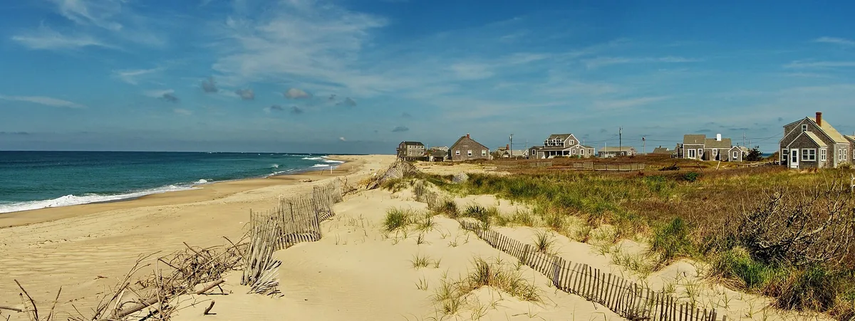 Sandy Atlantic beach and fenced dunes on Nantucket with grey-shingled houses on the bluff