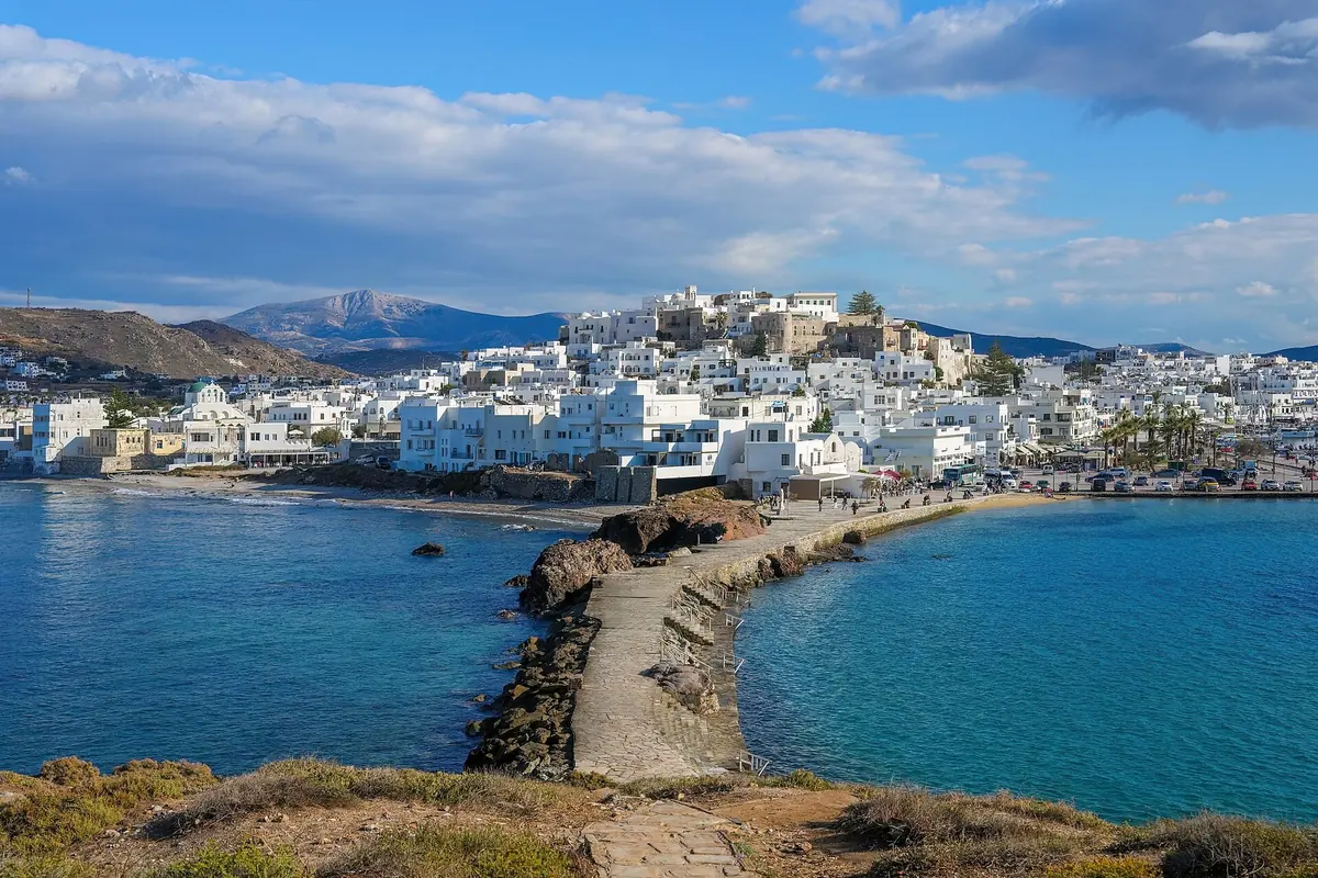 Naxos Town's white houses and hilltop castle seen from Palatia islet, with the stone causeway and harbour in front