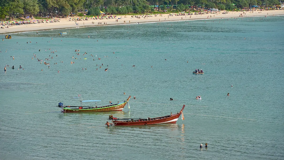 Longtail boats moored in the calm water off the long sandy curve of Kata Beach on Phuket