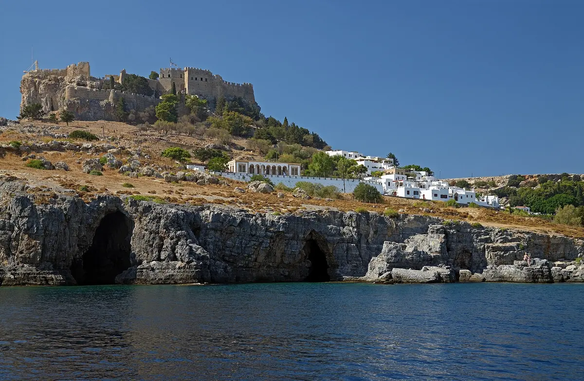 The acropolis of Lindos on its clifftop above sea caves and the white village houses, Rhodes