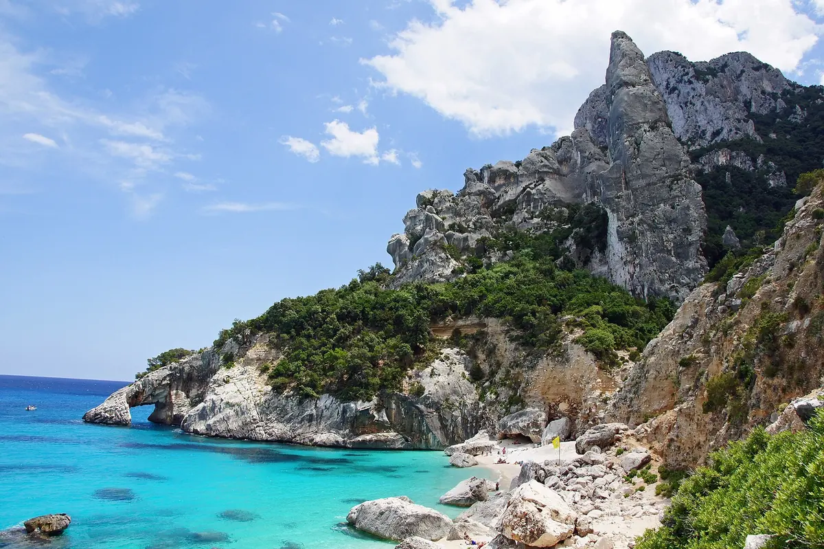 Turquoise water and white pebbles at Cala Goloritzé on Sardinia's east coast, below a limestone pinnacle and rock arch
