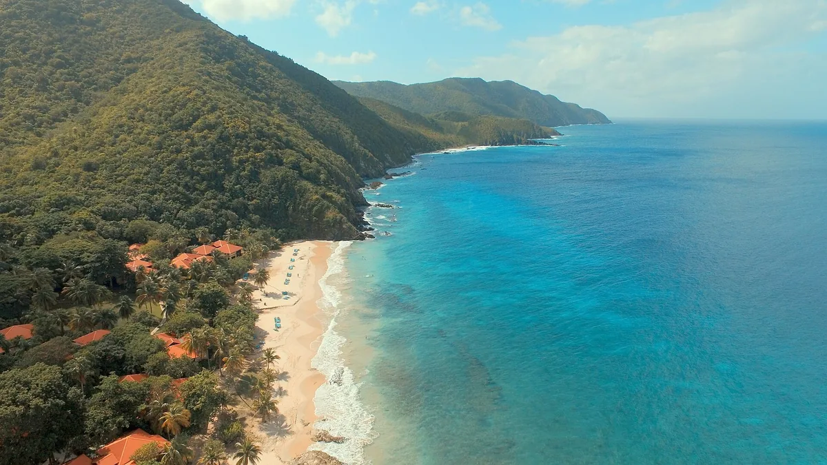 Forested hills dropping to a turquoise sea and a narrow sandy beach on the northwest coast of St. Croix