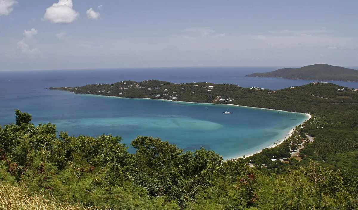 The white sand crescent and calm blue water of Magens Bay on St. Thomas, seen from the green hillside above